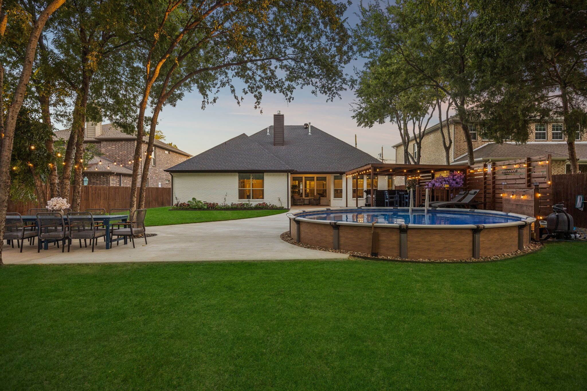 A backyard with a swimming pool, a covered patio, and a dining area.