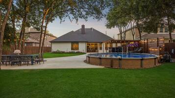 A backyard with a swimming pool, a covered patio, and a dining area.