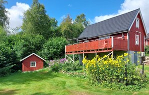 Ein rotes Bauernhaus mit einem Balkon, umgeben von üppigem Grün und blühenden Pflanzen.