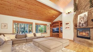 Una sala de estar acogedora con un sofá modular, una chimenea y grandes ventanales con vistas a un bosque.