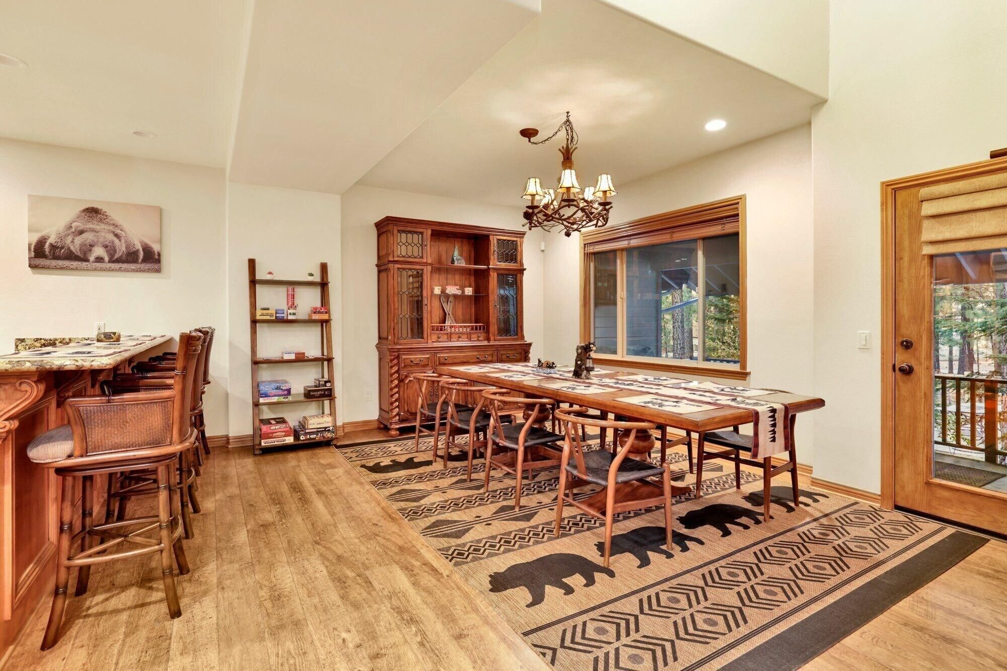 A dining room with a long wooden table, chairs, a chandelier, and a rug with animal silhouettes.
