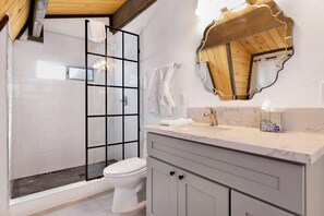A bathroom with a glass shower enclosure, a white toilet, a marble sink, and a wooden-framed mirror. - Bear Cabin #1976 (Big Bear Lake)