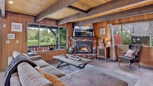 Una sala de estar acogedora con chimenea, asientos cómodos y grandes ventanales con vistas al exterior.