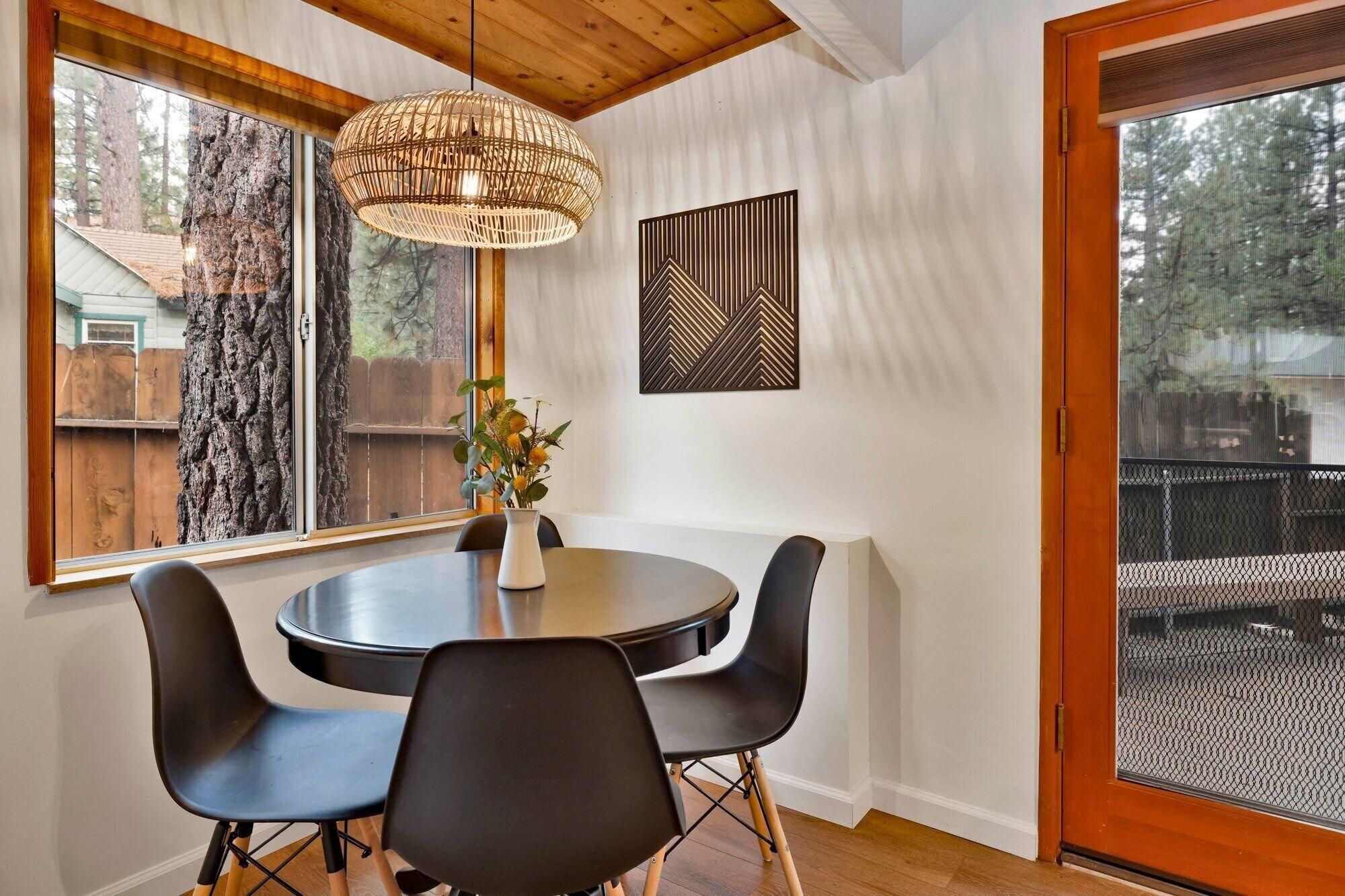 A dining area with a round table, two chairs, a hanging light fixture, and a view of a tree through a window.