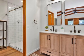 A bathroom with a glass shower enclosure, wooden vanity with two sinks, and a mirror above the vanity. - The Lost Compass #2165 (Big Bear Lake)
