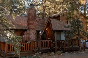 A cabin with a brick chimney, wooden deck, and a covered porch. - The Lost Compass #2165 (Big Bear Lake)