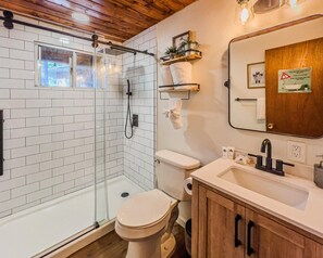 A bathroom with a glass-enclosed shower, a toilet, a sink with a mirror, and a wooden cabinet. - The Lost Compass #2165 (Big Bear Lake)