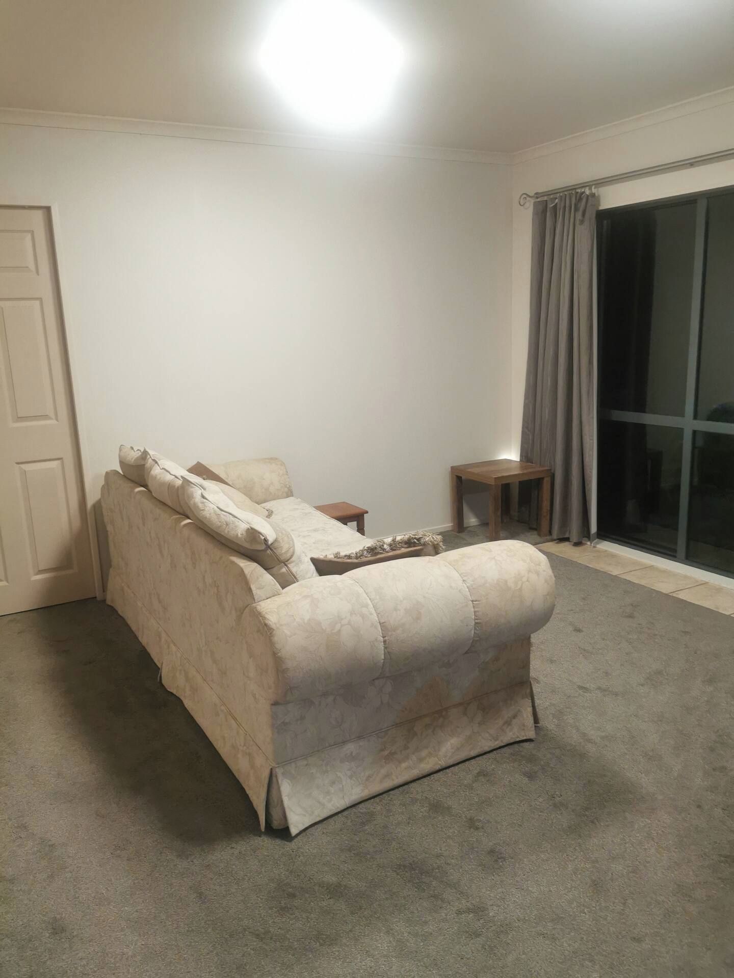 A room with a beige sofa, a small wooden side table, and a large sliding glass door with curtains.