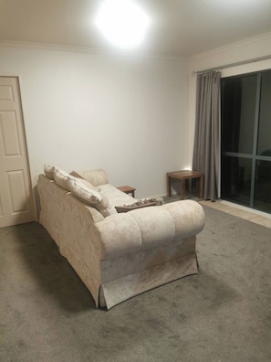 A room with a beige sofa, a small wooden side table, and a large sliding glass door with curtains.