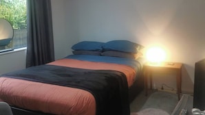 Ein Schlafzimmer mit einem Bett, einem Schreibtisch, einem Sessel, einer Lampe und einem Fenster mit Vorhängen.