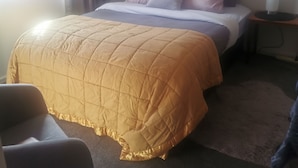 Ein Bett mit gestepptem Kopfteil, ein Nachttisch mit Lampe und ein Sessel.
