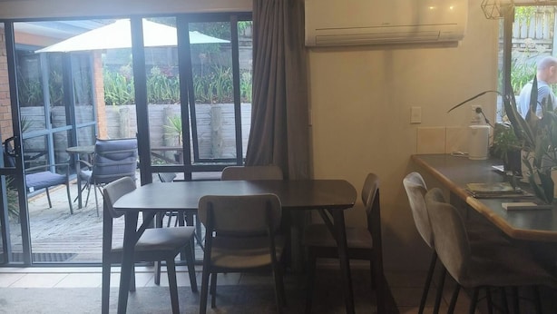 Ein Essbereich mit Tisch und Stühlen, eine Klimaanlage an der Wand und Blick durch große Fenster.