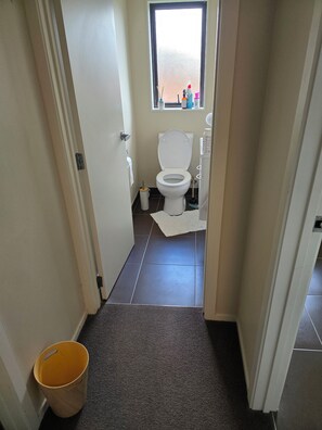 Ein schmaler Flur, der zu einem Badezimmer mit Toilette, Fenster und Mülleimer führt.
