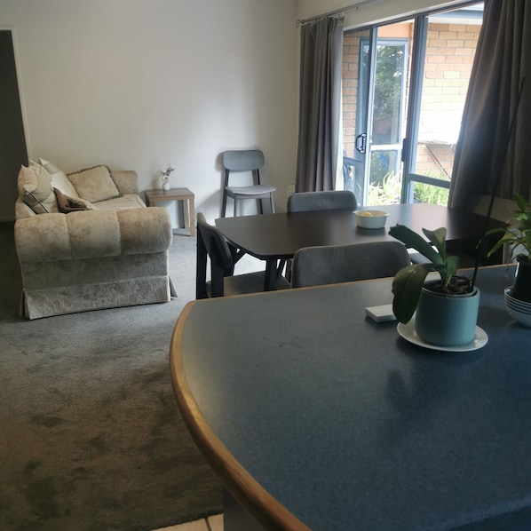 A living room with a sofa, a dining table, chairs, a small table with a vase, and a window with curtains.