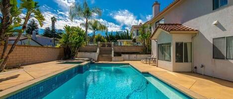 A swimming pool with a clear blue water, surrounded by a patio area with steps leading to a house.