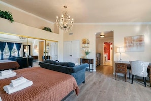 A hotel room with a large bed, a sofa, a desk, and a chandelier.
