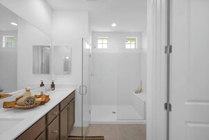 Un baño moderno con ducha envuelta en vidrio, un espejo grande y un tocador con artículos de aseo.