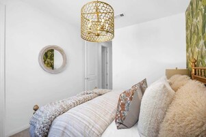 Un dormitorio con cama, un espejo redondo, una puerta y una lámpara de pared.