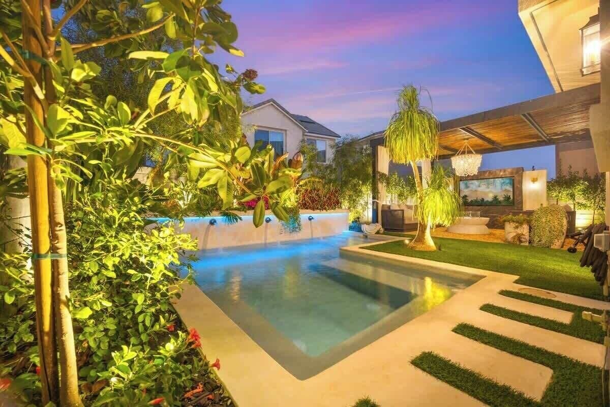 A modern outdoor pool area with a clear pool, surrounded by greenery and a well-maintained lawn.