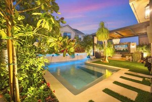 Un área de piscina moderna al aire libre, con agua cristalina, rodeada de vegetación y un césped cuidado.