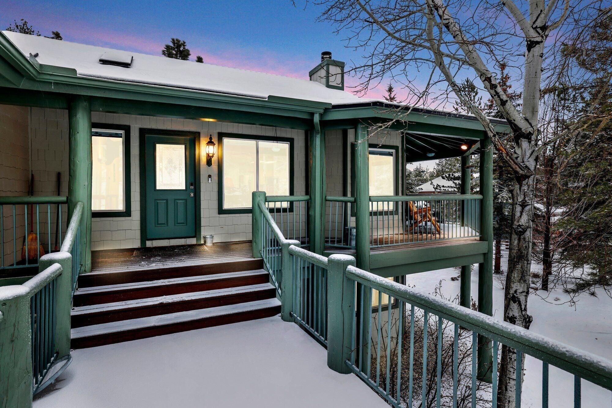 Un edificio cubierto de nieve con fachada verde, una puerta principal y una escalera que lleva a un balcón.