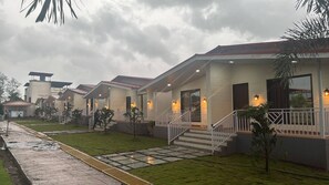A row of modern hotel buildings with individual entryways, each with a small porch and steps leading to the entrance. - Peak Paradise Resort (Karjat)