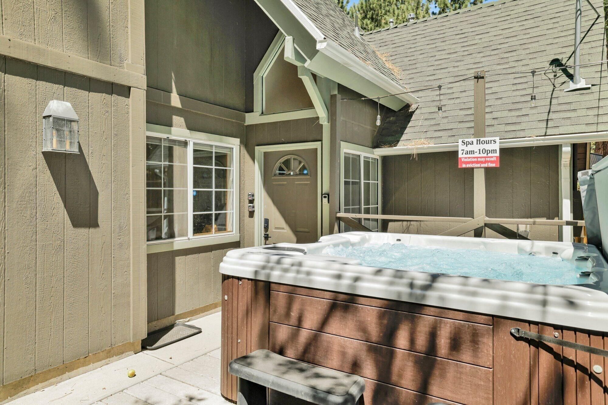 A hot tub with a wooden exterior, a sign indicating spa hours, and a window with a view of the outdoors.