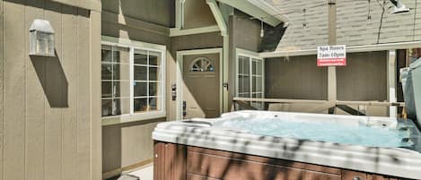 A hot tub with a wooden exterior, a sign indicating spa hours, and a window with a view of the outdoors.