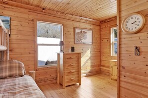 Habitación de cabaña de madera con cama, cómoda, reloj y un cuadro enmarcado de un leopardo.