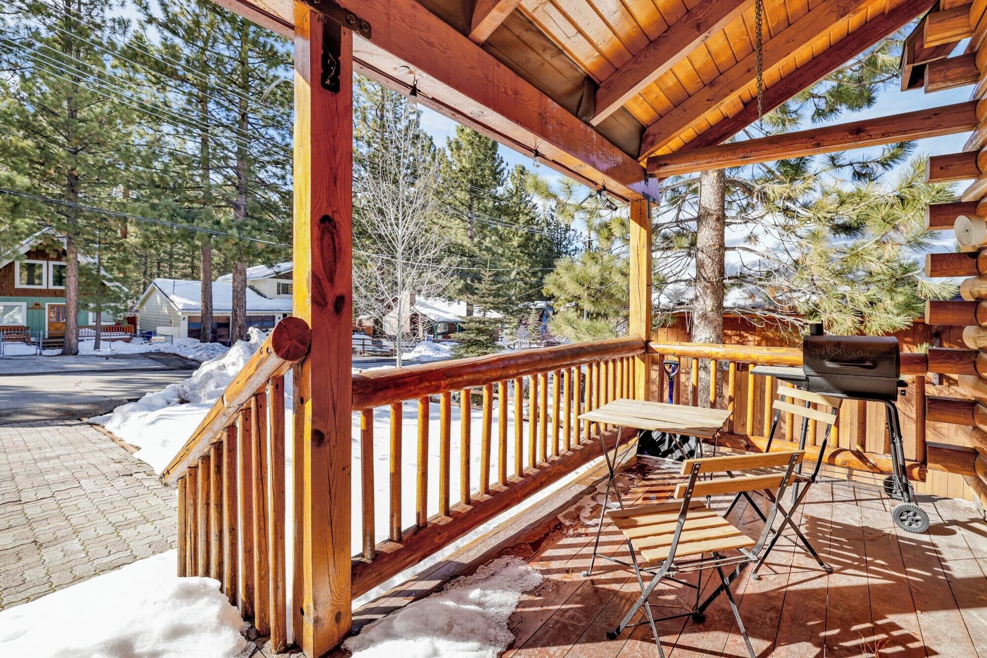 A wooden deck with a bench and a grill, surrounded by trees and a snowy landscape.
