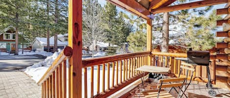 A wooden deck with a bench and a grill, surrounded by trees and a snowy landscape.