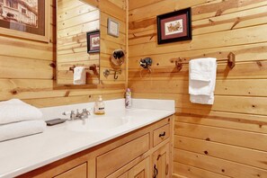 Un baño estilo cabaña de madera con lavamanos, espejo, toallero y cuadros en la pared.
