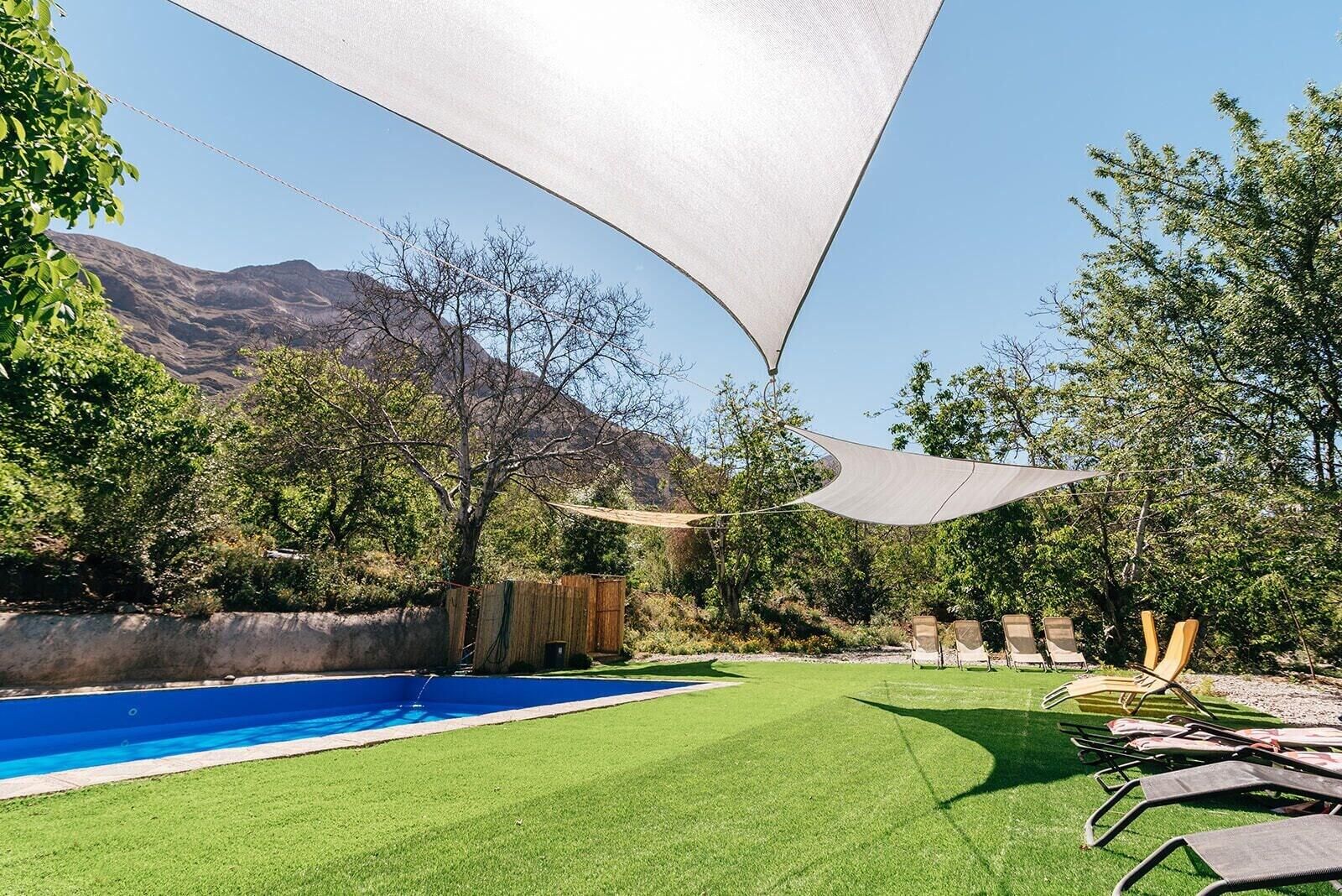 A backyard with a swimming pool, lawn chairs, and a large shade sail.