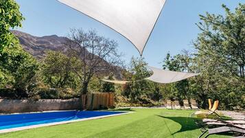 A backyard with a swimming pool, lawn chairs, and a large shade sail.