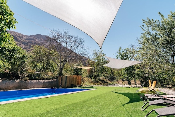 A backyard with a swimming pool, lawn chairs, and a large shade sail.