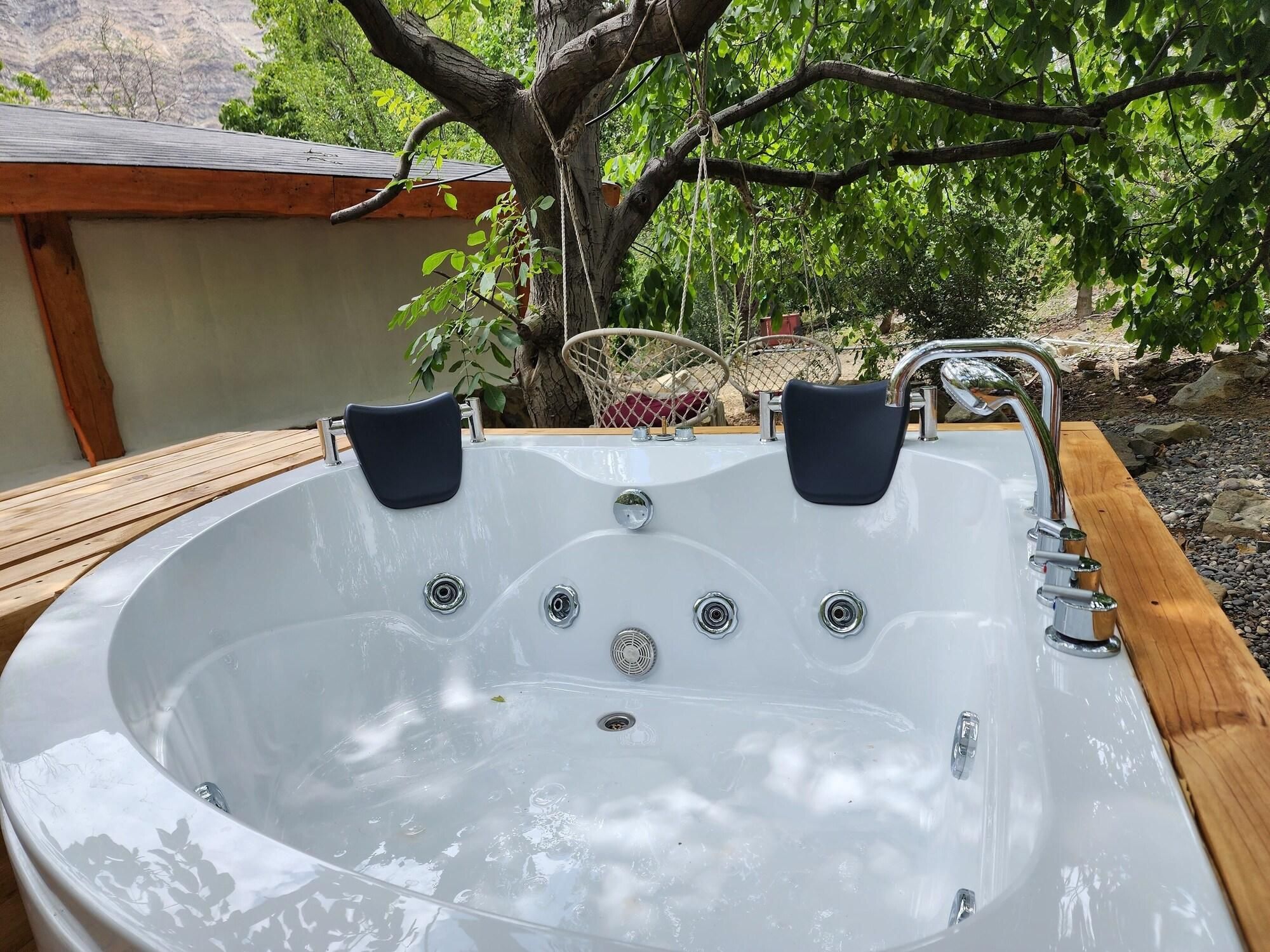 A hot tub with two chairs, surrounded by a wooden deck and a tree.