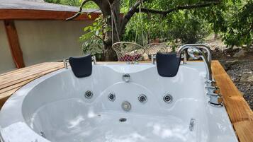 A hot tub with two chairs, surrounded by a wooden deck and a tree.
