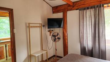 A room with a bed, a standing fan, a television, and a wooden shelf unit.