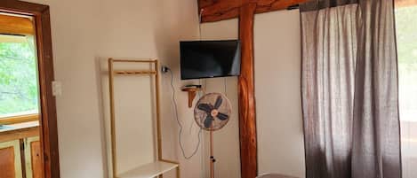 A room with a bed, a standing fan, a television, and a wooden shelf unit.