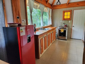 A compact kitchen with a refrigerator, stove, sink, and wooden cabinets.