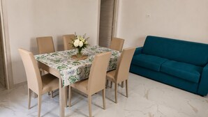 Een eetruimte met een tafel voor vier personen, omringd door stoelen, en een turquoise bank tegen de muur.