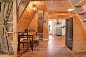 A cozy wooden interior with a dining area, kitchen, and a visible door leading to another room. - Whispering Woods #2375 (Big Bear Lake)