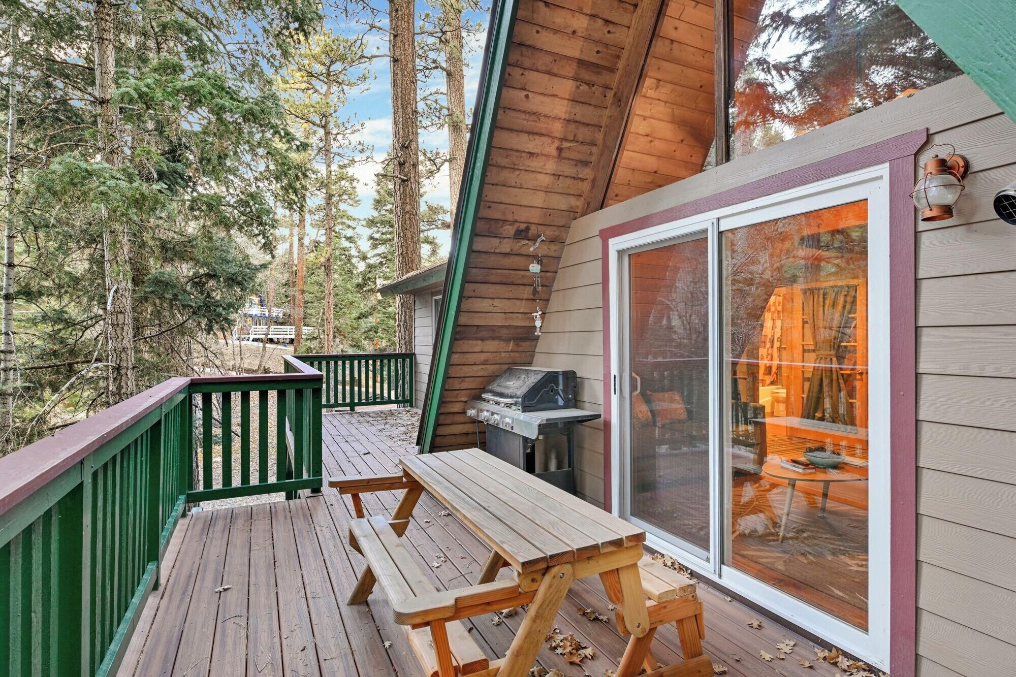 Um deck de madeira com mesas de piquenique, churrasqueira e uma porta de vidro que dá para o interior.