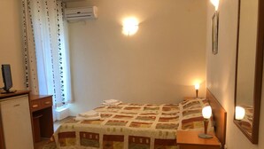 Un dormitorio con cama, lámparas de noche, escritorio, silla, refrigerador pequeño y ventana con cortinas.
