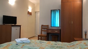 Habitación de hotel con cama, escritorio, armario, televisor y ventana con cortinas.