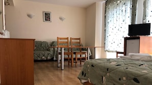 Una habitación de hotel con una cama, un escritorio de madera, una silla, un televisor y una ventana con cortinas.