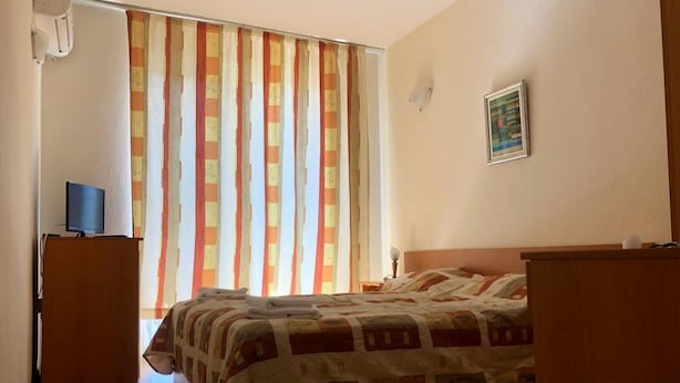 Un dormitorio con cama, escritorio, silla, televisor y ventana con cortinas.