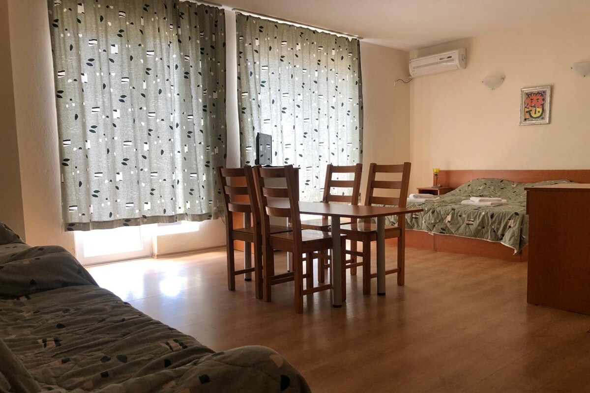 Una stanza con un letto, un tavolo con sedie, una scrivania e una finestra con tende.