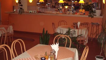 A restaurant interior with a bar area, tables with chairs, and potted plants.