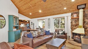 Una sala de estar acogedora con chimenea, una cocina al fondo y un ventanal grande.